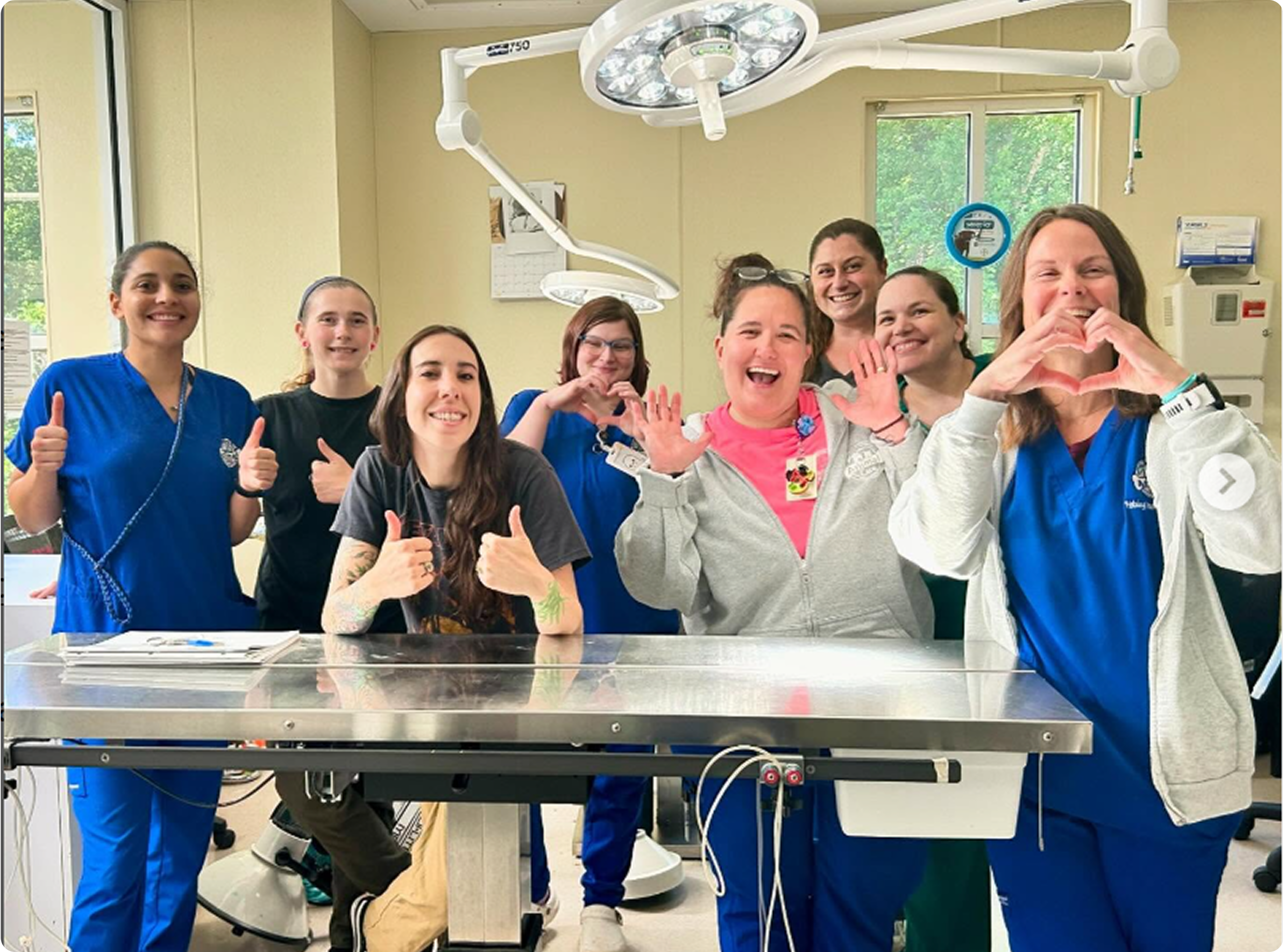 Group of people in a medical setting, posing with thumbs up and heart shapes.