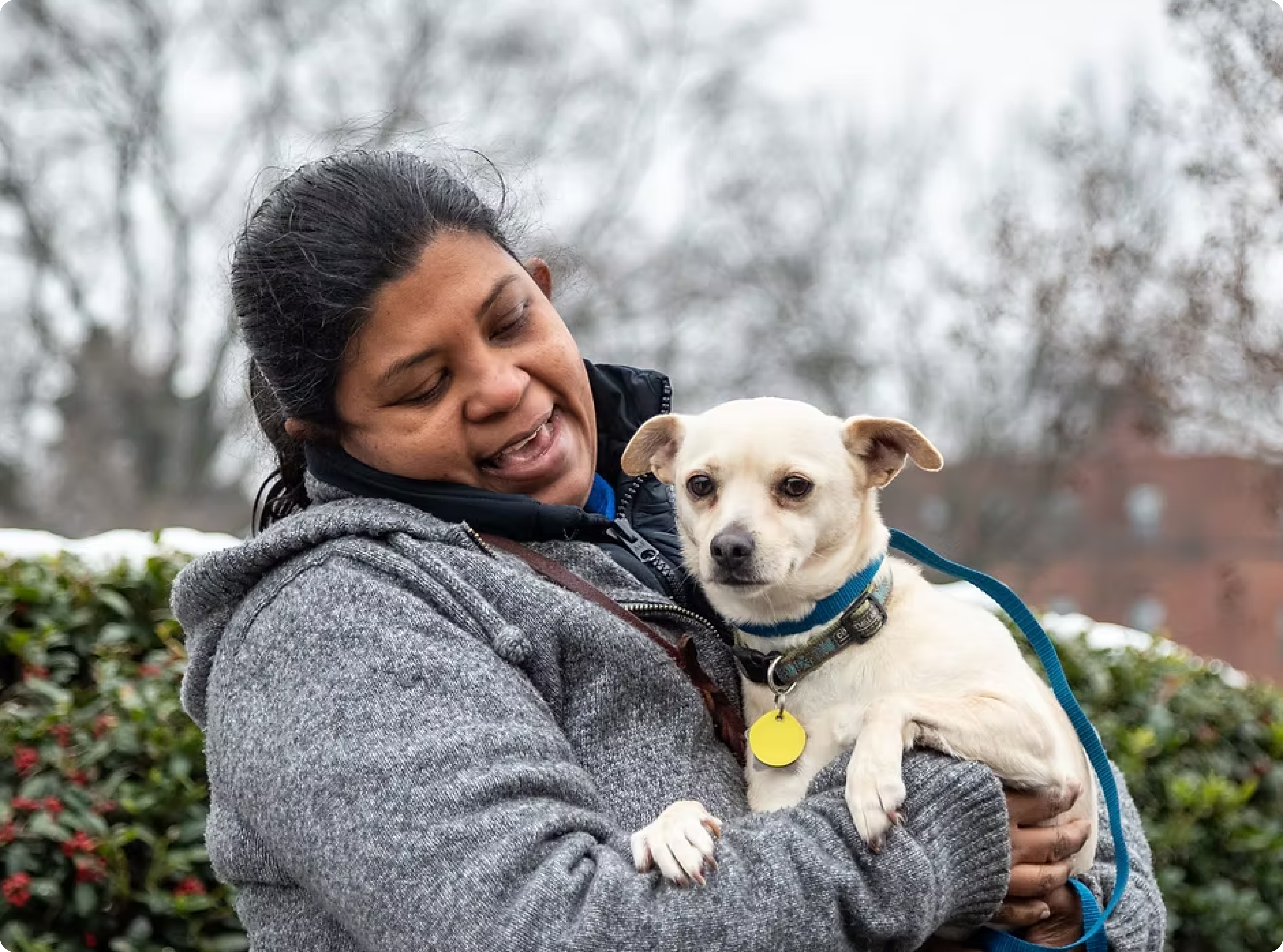 Woman holding a small white dog outdoors with blurred background