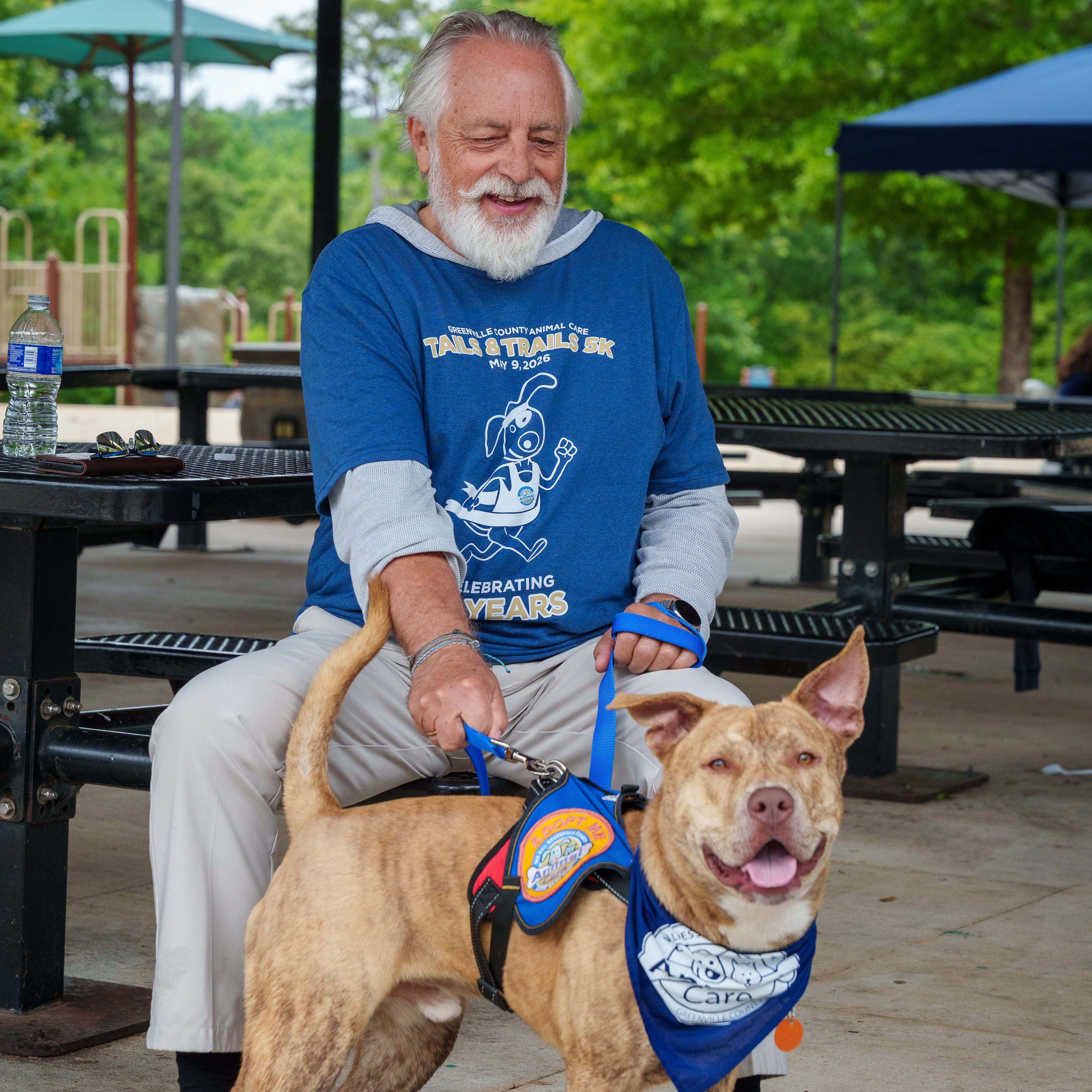 Man sitting with a dog on a leash at an outdoor setting