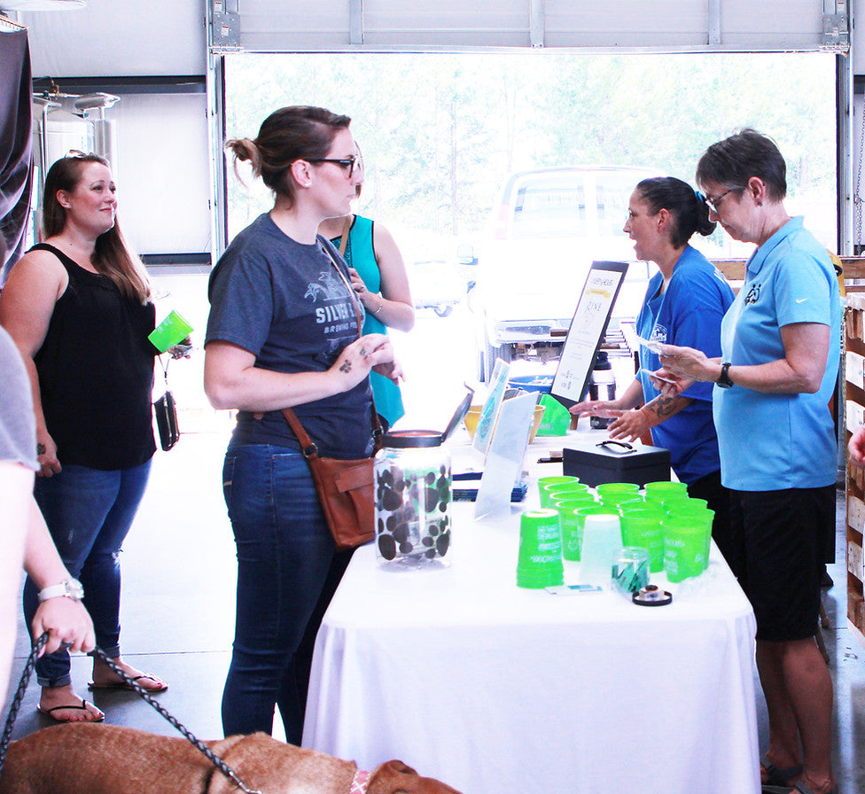 People interacting around a table with green cups at an event.
