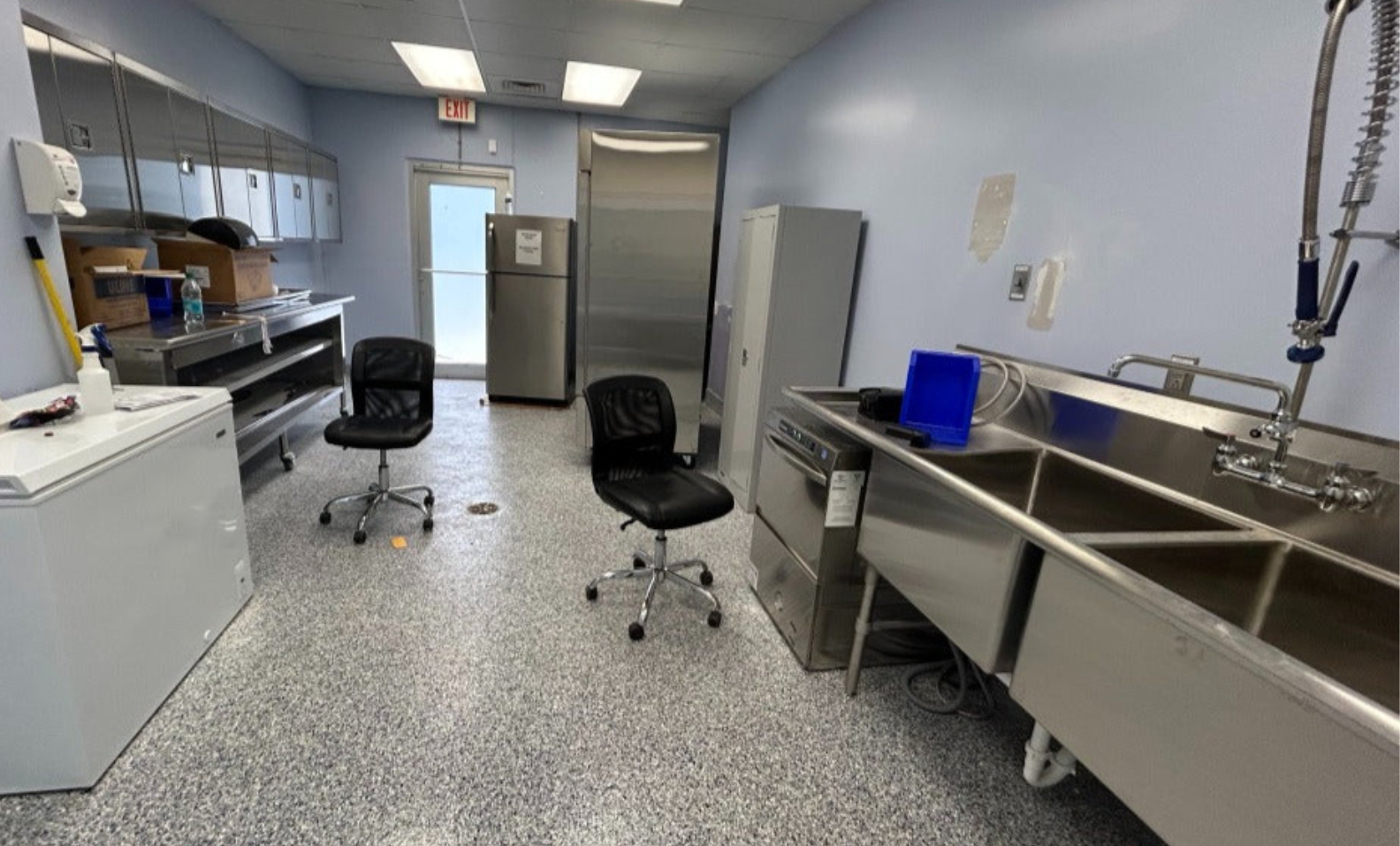 Laboratory or kitchen with stainless steel counters, chairs, and appliances.
