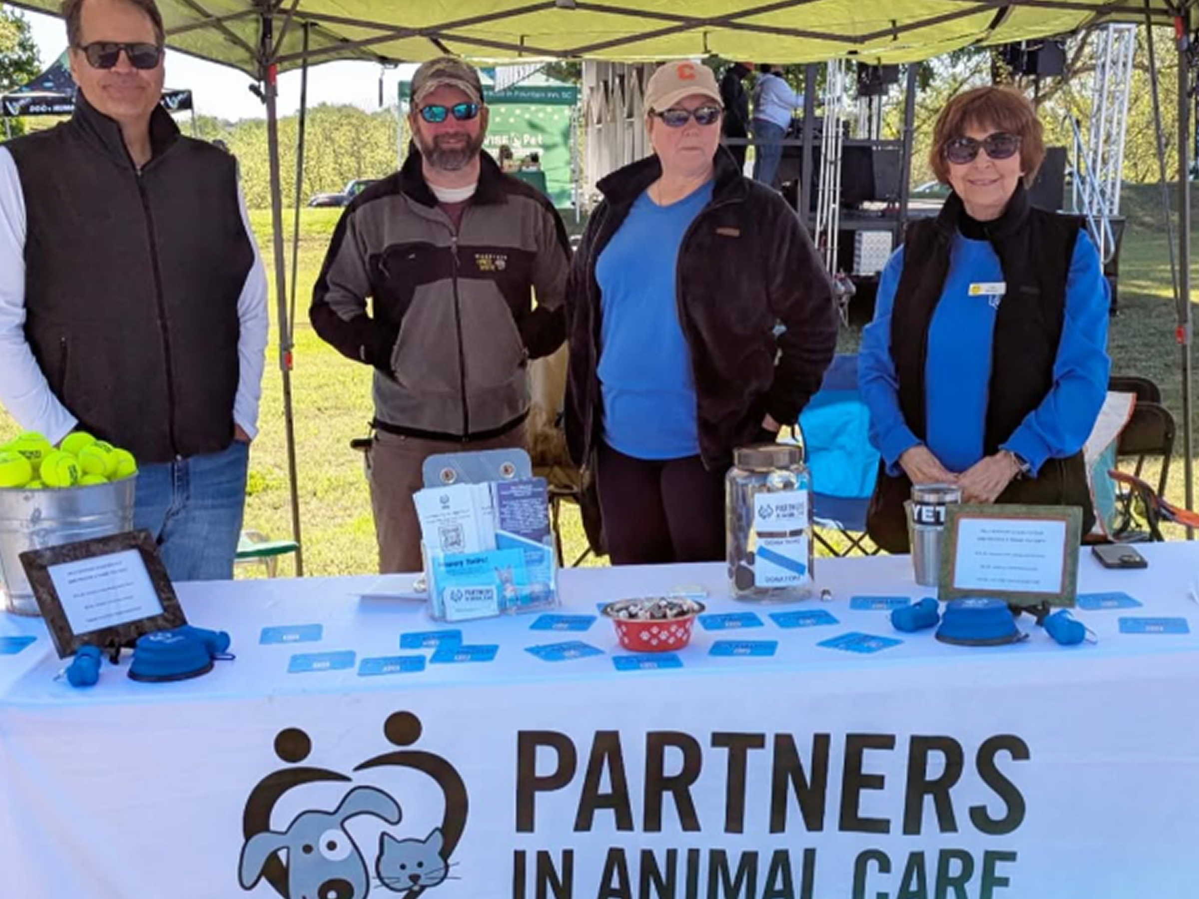 Group of people standing behind a table with 'Partners in Animal Care' branding at an outdoor event.